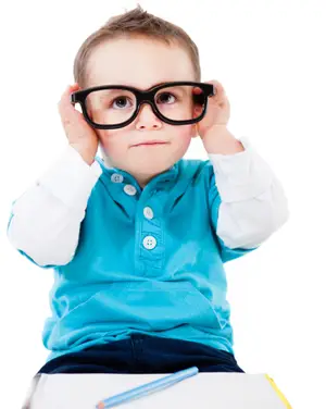A young boy wearing glasses and a blue shirt is holding his glasses up to his eyes.