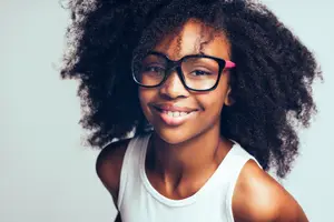 A smiling young girl with curly hair and black glasses posing for a photo