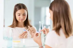 Two women are brushing their teeth in front of a mirror.