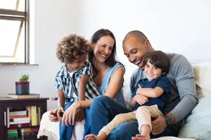 A family sitting on a couch with two children smiling and looking at the camera.