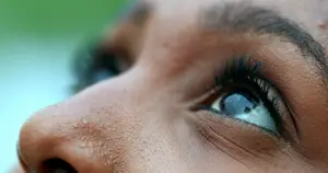 Close-up of a woman's face with brown skin, black eyelashes, and brown eyes, slightly tilted upwards with a green background.