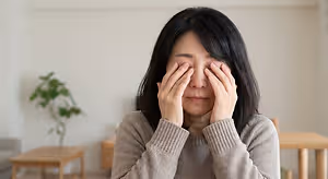 an older Asian woman sitting at a table with her hands covering her face