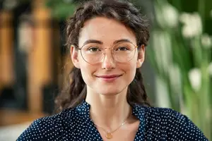 woman wearing a blue polka dot shirt and gold glasses smiling at the camera