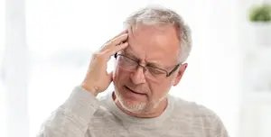 Older man with white hair wearing glasses holds head in pain
