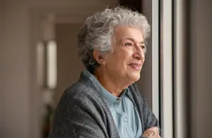 Elderly woman standing by a window with a warm smile on her face
