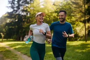 A man and woman are jogging in a park, smiling and holding a water bottle.