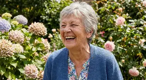 Older woman in blue cardigan standing in a garden laughing