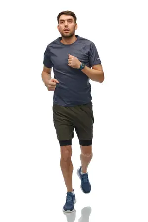 A man running while wearing a grey t-shirt, green shorts, and blue shoes.