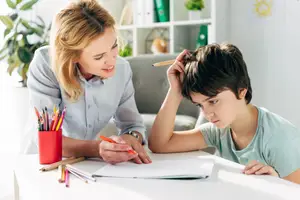 A woman is helping a boy with his homework by giving him some advice and pointing to his head.