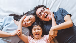A family of three lying on a bed, smiling and holding hands