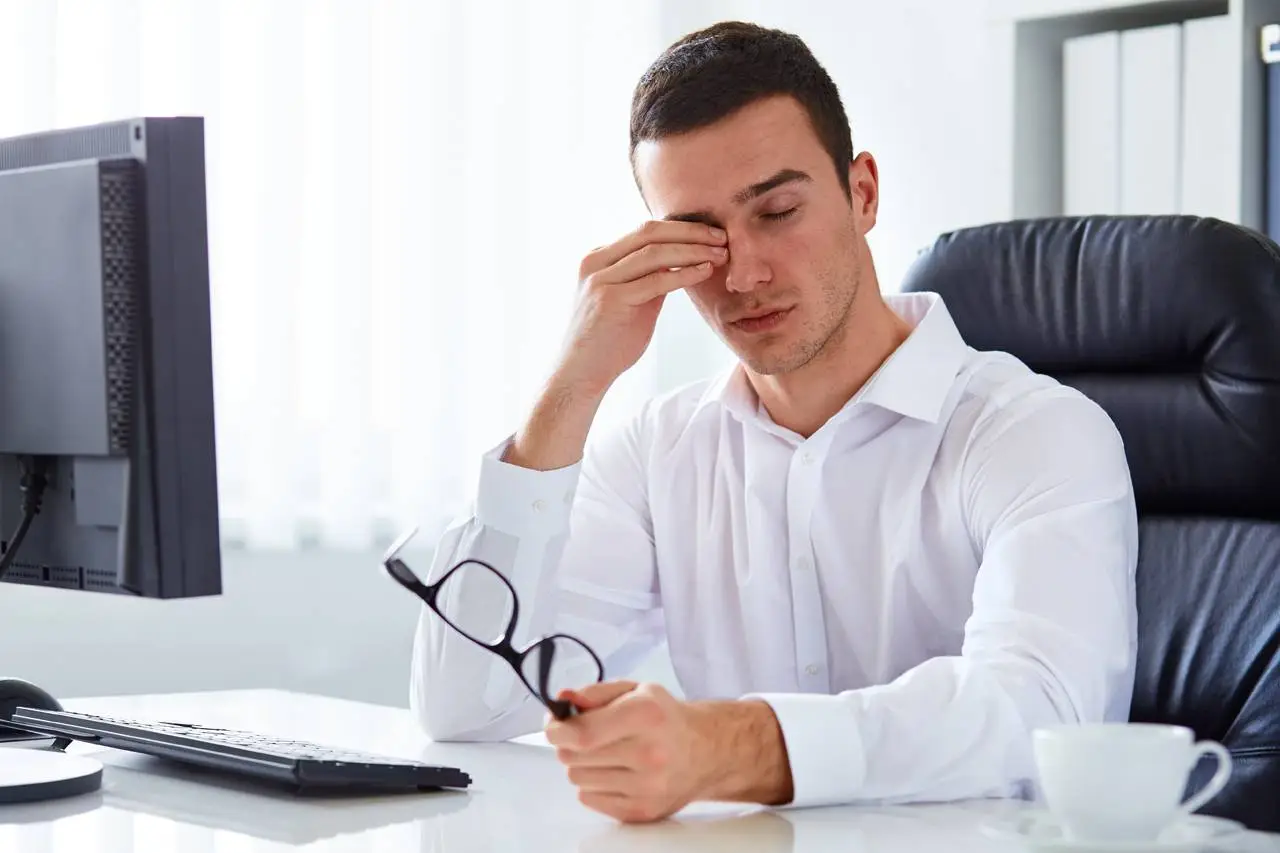 A man sitting at a desk with his hand on his face and looking at a computer monitor