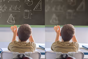 A boy sitting in a classroom with his hand raised to ask a question.