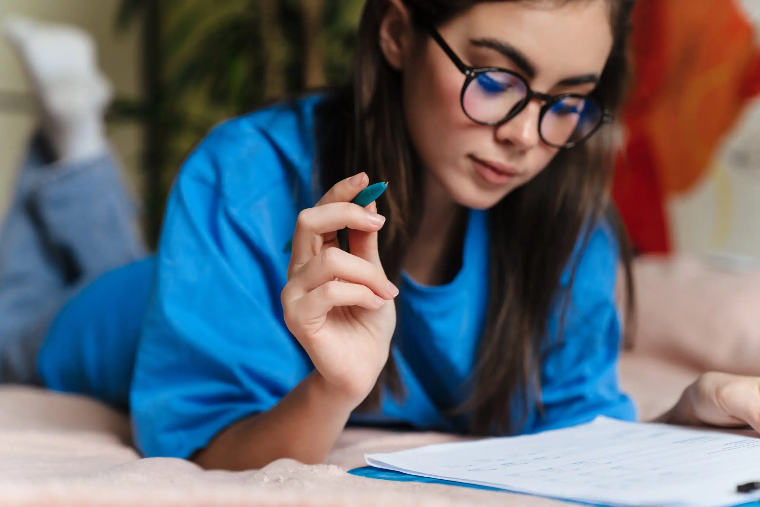 young girl in glasses doing homework on a bed