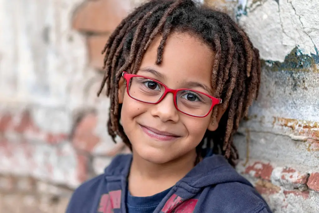 Portrait of a smiling young boy wearing glasses against a brick wall