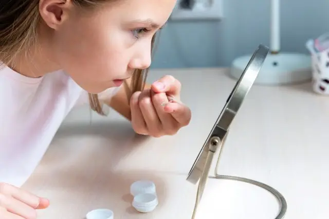 A young girl is holding a magnifying glass and looking at an object on a table