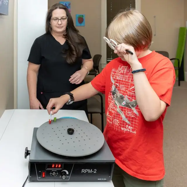 A boy is using a device to test his hearing with the help of a woman who is standing beside him.