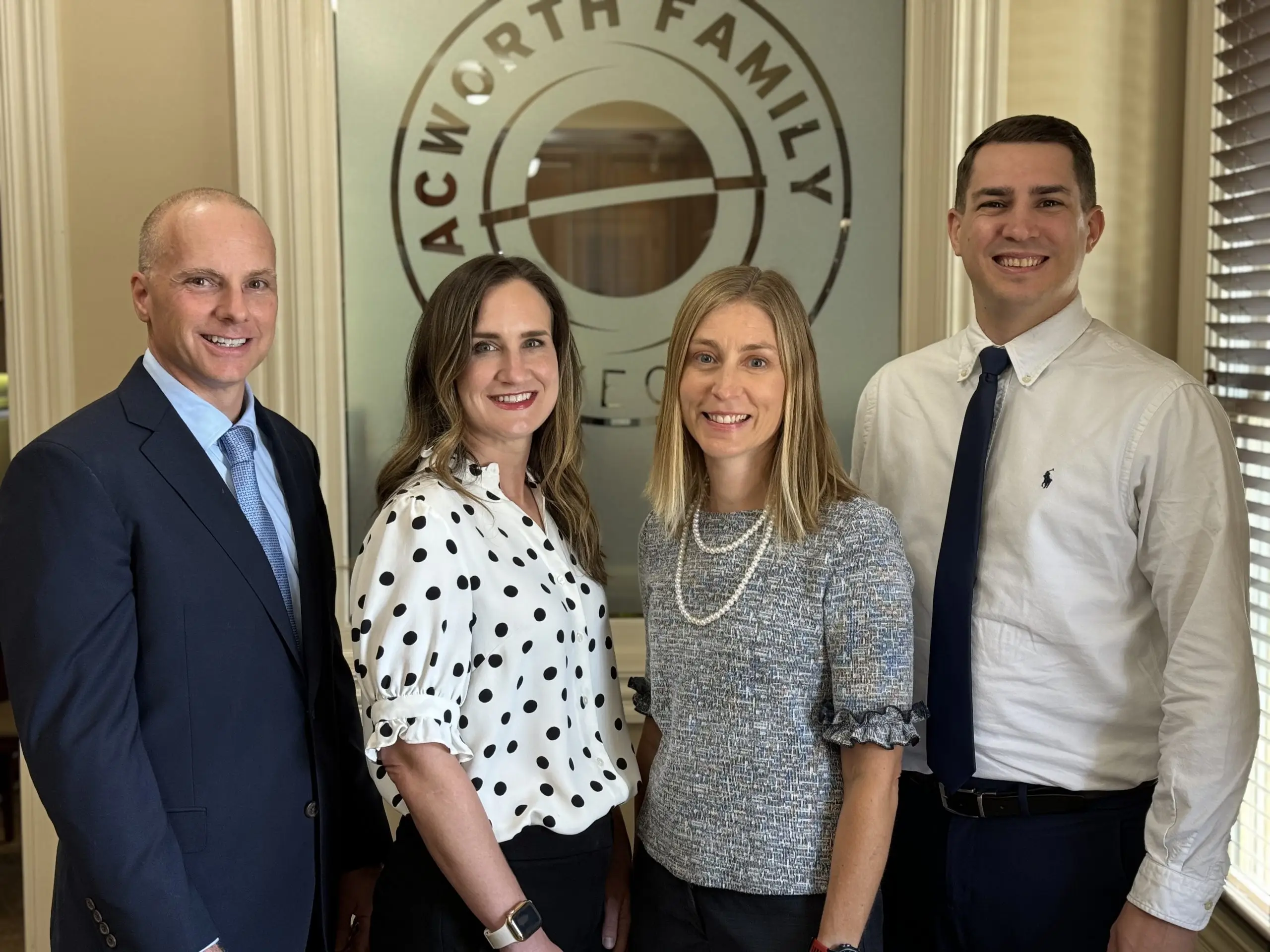 Four individuals, three women and one man, are smiling and posing for a photo in front of a sign that reads 'Acworth Family'