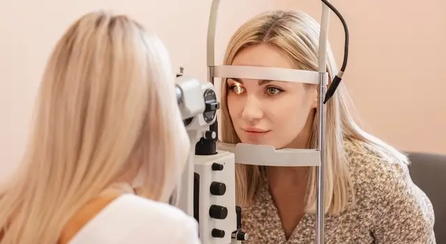 A woman undergoing an eye exam with an optometrist using a slit lamp.
