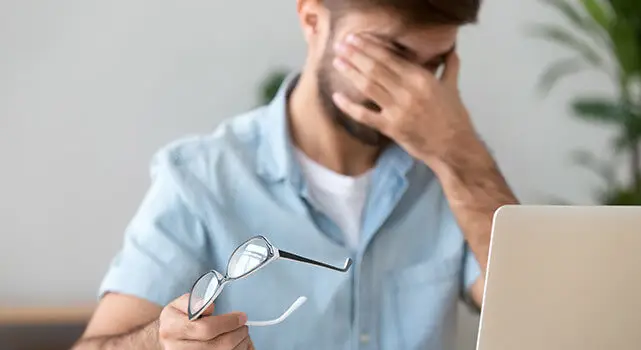 A man adjusting his glasses while covering his face with his hand, likely feeling stressed or overwhelmed.
