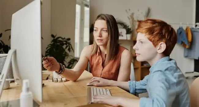a woman and a boy in front of a computer