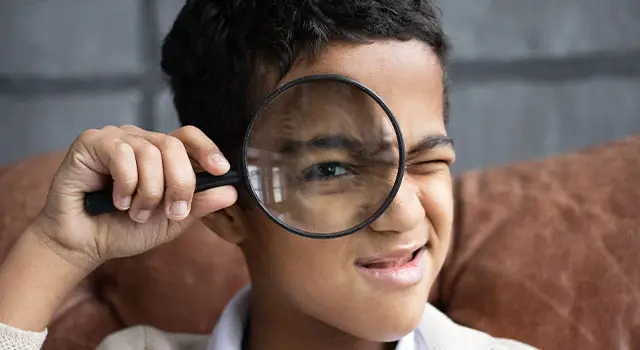 A boy is smiling while holding a magnifying glass in his hand