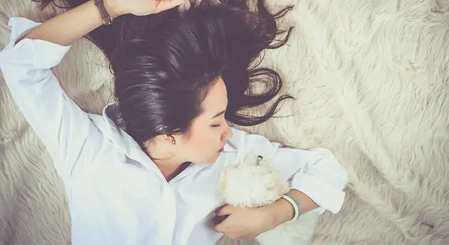 a woman with black hair lying on a white fur bed while holding a white fluffy stuffed animal in her hand