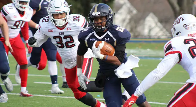 Football players from two teams are competing on a field, one player is running with a ball while others are chasing him.