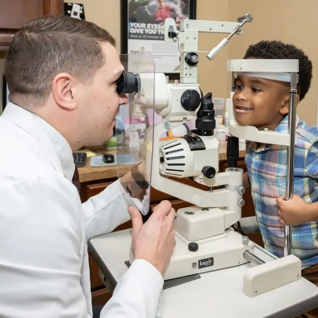 An eye doctor using a machine to check a young boy's vision.