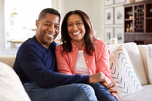 A man and woman sit together on a sofa and smile at the camera