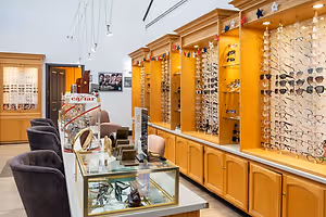 An eyeglass shop with wooden cabinets and a display case with many pairs of glasses, chairs, and a poster on the wall