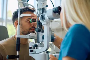 Patient having an eye examination with a slit lamp while an optometrist operates the equipment