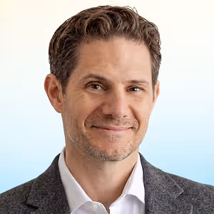 A headshot of a man in a suit and a white shirt smiling for the camera