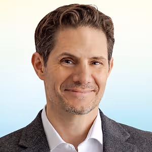 A smiling man in a grey blazer and white shirt