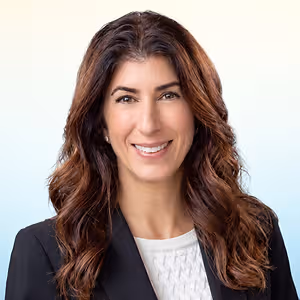 Headshot of a woman in a black blazer with long brown wavy hair