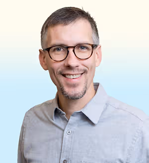 Man wearing glasses and a light gray shirt with a smile on his face