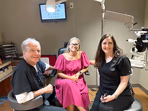 Three people sitting in a medical room with a monitor on the wall.