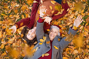 Two people lying on the grass and smiling while leaves are falling on them