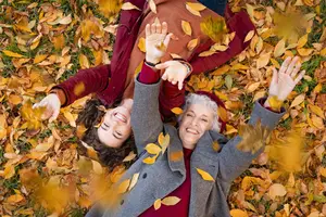 Two people lying on the grass and smiling while leaves are falling on them