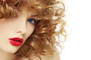 Close-up of a woman with curly hair, blue eyes, and red lipstick looking forward