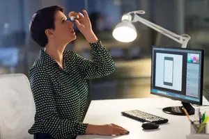 A woman sitting at a desk in front of a computer monitor using a nasal spray
