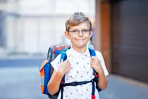 A young boy wearing glasses and a backpack, smiling at the camera.