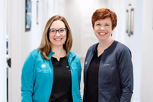 Two women in teal jackets smiling in a hallway