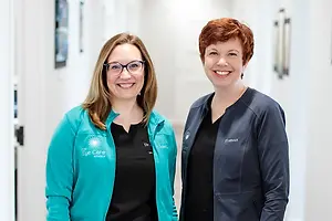 Two women in teal jackets smiling in a hallway