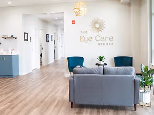 The Eye Care Studio waiting room has a couch, a plant, and a desk with a plant in the corner.