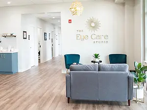 The Eye Care Studio waiting room has a couch, a plant, and a desk with a plant in the corner.