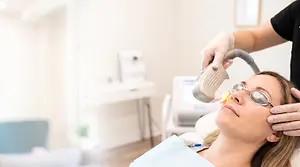 A woman is having laser treatment on her face by a professional in a clinic setting.