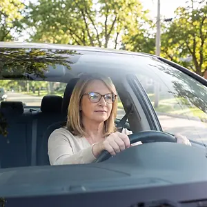 A woman with glasses drives her car on a sunny day