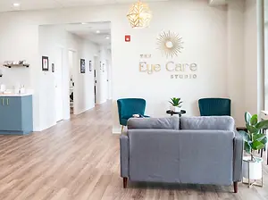 The Eye Care Studio waiting room has a gray sofa, blue chairs, and a wall logo.