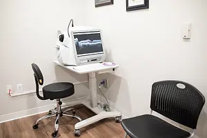 An ophthalmic examination room with a monitor, a black chair, and a desk with a white mouse on top