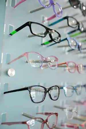 An array of colored eyeglasses are displayed on a blue wall.